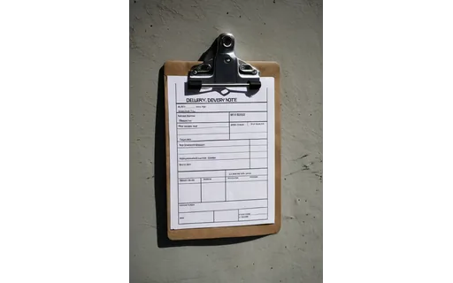 A delivery note on a clipboard held against a van door, outdoor overcast light, slight angle